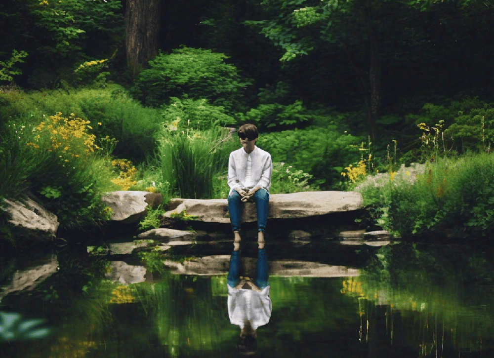 A person sitting by a peaceful pond, with a clear reflection